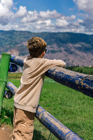 Smiling Colombian boy in yellow shirt standing in front of old brick wall, holding a plant pot with a green seedling, environmental careの写真素材