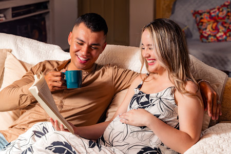 Colombian adult couple in love, pregnant Caucasian adult woman reading a book with her husband,...