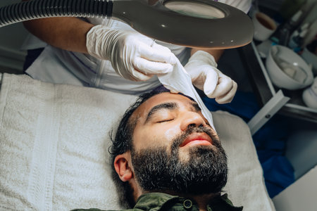 photo of professional exfoliation, moisturizing and facial cleansing treatment for a bearded Colombian mestizo adult male with moisturizing gel covering his eyes.の写真素材