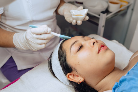 Photo of a young Colombian mestiza girl in a beauty spa where she is having a facial cleansing and is going through the step of applying a moisturizing gel on her face.の写真素材