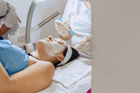 Copy-spaced photo of dermatologist applying mud mask to face of young adult Colombian Latina woman...
