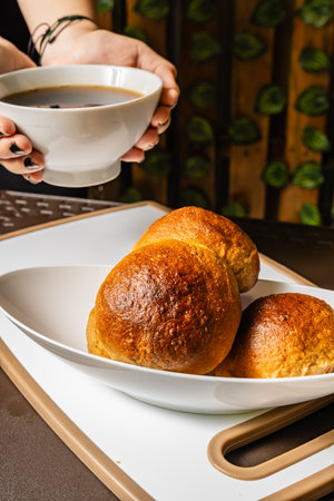 vertical photo of traditional handmade whole wheat mogolla breads next to a woman holding a cup of...