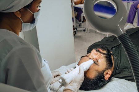 Photo of a bearded mixed-race Colombian man at a beauty spa where a facial cleansing is performed and the dermatologist goes through the purification step with a facial microcurrent device.の写真素材