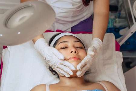 Photo of a young Colombian mestiza woman in a beauty spa where she massages her face with a moisturizing product in a facial cleansing treatment.の写真素材