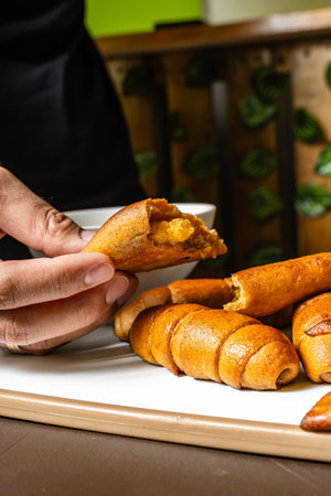 vertical photo of adult man's hands opening whole wheat empanada with pineapple inside, whole wheat cheese sticks, next to cup of coffee in healthy vegetarian restaurant in Colombia.の写真素材