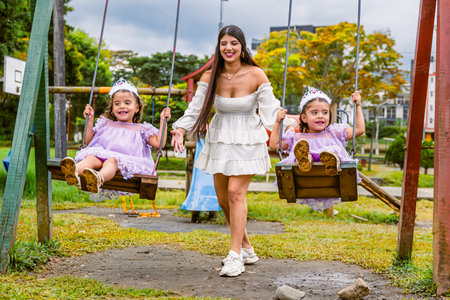 Mother plays with twin daughters on swings during outdoor birthday celebration in parkの写真素材