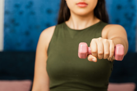 Close-up of Colombian woman's arm lifting pink dumbbell against patterned blue wall with copy space.の写真素材