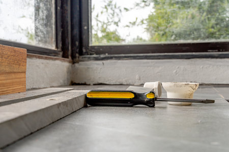Flathead screwdriver and PVC pipe fittings on tiled floor near window corner, capturing home improvement tools and materials in a casual renovation workspace.の写真素材