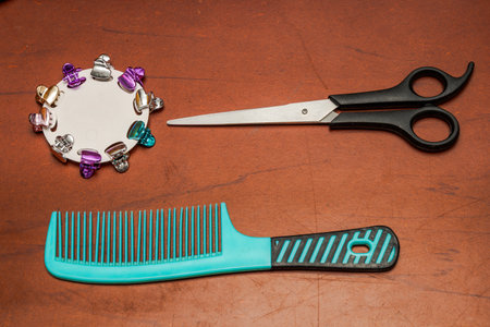 Scissors, comb, mirror, and colorful hair clips arranged on reddish surface, showcasing personal grooming tools in a playful and organized beauty setup.の写真素材
