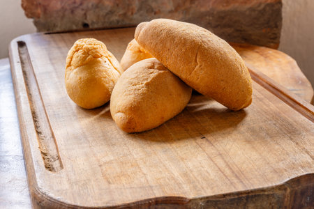 Four pieces of rustic bread with golden crust on wooden cutting board, featuring round and oval...