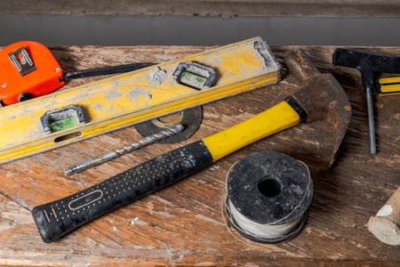 Assorted construction and carpentry tools on wooden surface, including hammer, spirit level, tape...