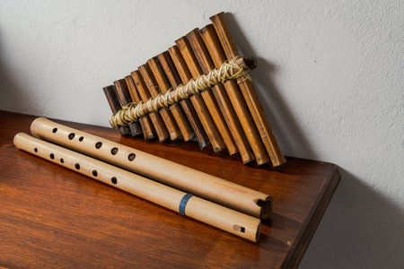 Traditional bamboo flutes and pan flute on wooden surface against white wall, showcasing handmade...