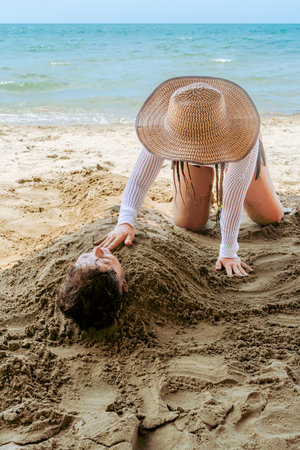 Colombian aunt shaping sand over buried nephew at Caribbean beach, playful moment in CoveÃ±as.の写真素材