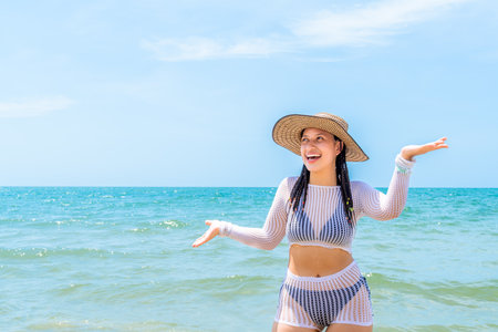 Caribbean woman smiles with both hands raised in playful surprise at the tropical beach, wearing a mesh outfit under the sun and facing the sea.の写真素材