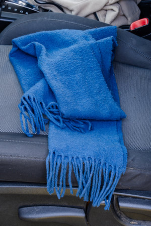 Blue woolen scarf with fringes resting on car seat.