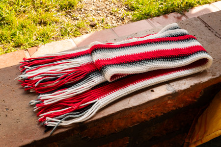 Striped handmade scarf with fringes resting on brick ledge in sunlit outdoor setting.