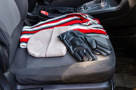 Striped scarf, gloves, and beige cap arranged on front car seat for winter travel.
