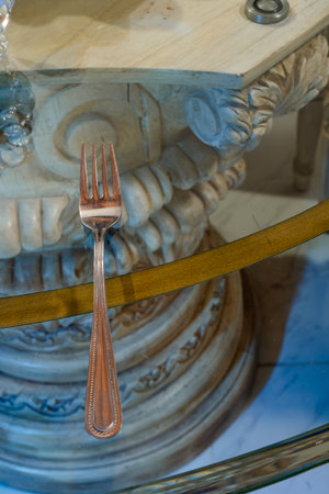 Ornate fork on glass table with carved classical base and golden-green accent.の写真素材