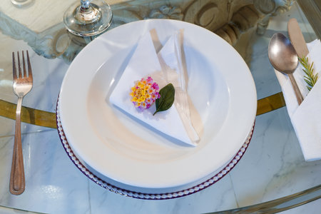 Elegant table setting with floral napkin and rosemary-wrapped silverware on glass and marble base.の写真素材