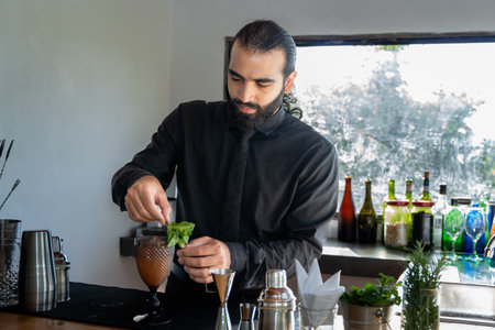 Bartender garnishing cocktail with mint in hotel bar with foggy windowの写真素材
