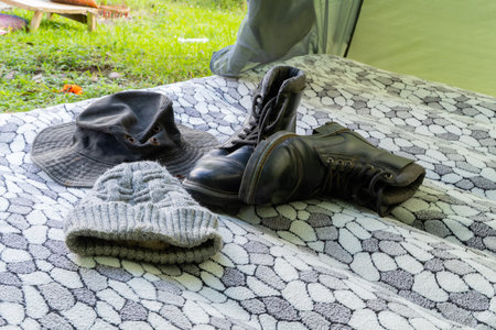 Camping gear including boots, hat, and beanie on patterned blanket inside tentの写真素材