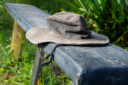 Worn gray wide-brimmed hat with chin strap resting on weathered bench in outdoor setting