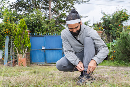 Person tying shoelaces in garden with blue gate and green plantsの写真素材