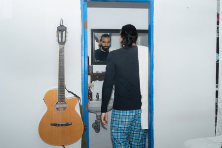 Man in bathroom with towel over shoulder looking into mirror in domestic settingの写真素材