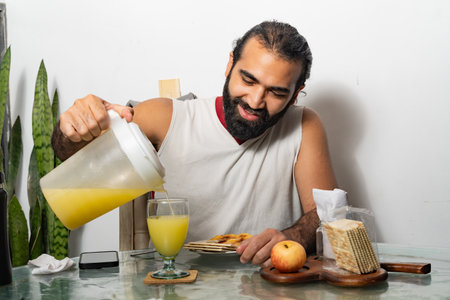 Person smiling while pouring juice at breakfast table with food and smartphoneの写真素材