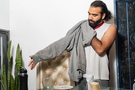 Person putting on sweatshirt beside glass table after eating Colombian arepa.の写真素材