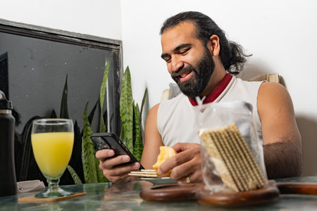 Person smiling at phone while eating arepa and crackers at glass table.の写真素材
