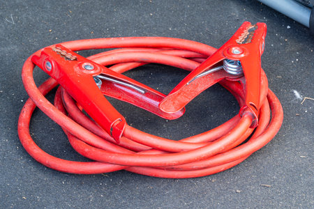 Red jumper cables with alligator clips coiled on dark surface for vehicle useの写真素材