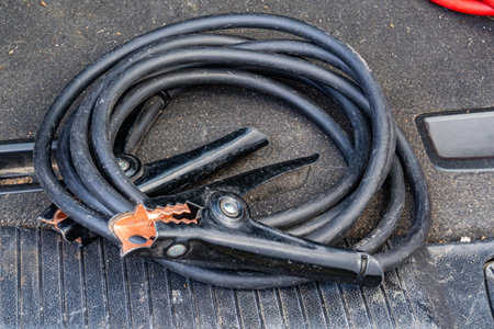 Black jumper cables with copper clamps placed on textured car floor matの写真素材
