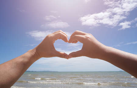 two hands male and female in heart shape at beach, On a cloudy sky background, romantic dayの写真素材