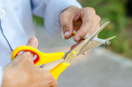 A hand hold cigarette being cut with scissorsの写真素材