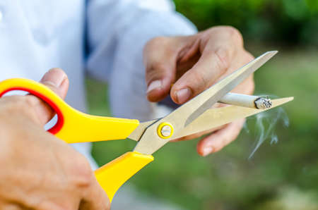 A hand hold cigarette being cut with scissorsの写真素材
