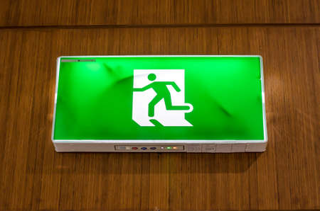 Illuminated green exit sign suspended from the ceiling in a public transportation facility. Signage consists of a human figure runningの写真素材
