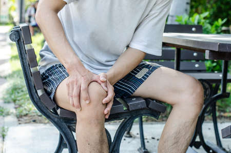 Man holding right knee with both hands while sitting down to show pain in the knee areaの写真素材