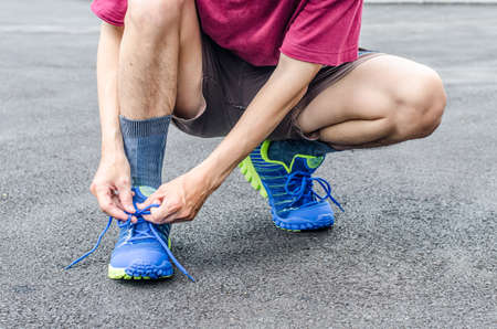 Male athlete tying laces for jogging on road in the parkの写真素材