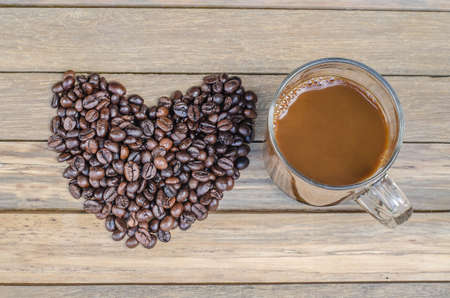 Cup with coffee and heart of coffee beanes on wood backroundの写真素材