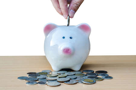Saving, male hand putting a coin into piggy bank and money on table.の写真素材
