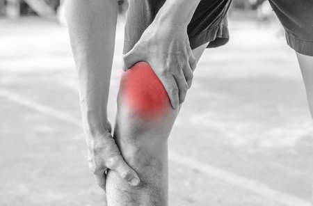 young sport man with strong athletic legs holding knee with his hands in pain after suffering ligament injury during a running workout training isolated on white background in black and whiteの写真素材