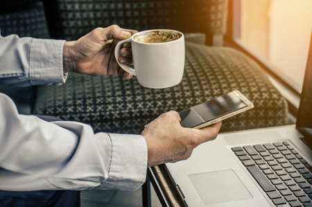 Young hipster guy texting with his mobile phone at the bar and having a cappuccino.Young man drinking espresso coffee in city cafe during lunch time and working on tablet computerの写真素材