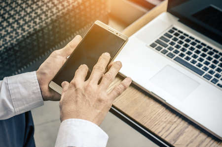 young man working from coffee shop using smart phone and notebook computer, man's hands using smart phone in interior.の写真素材