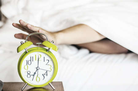 sleeping asian young male disturbed by alarm clock early morning on bedの写真素材