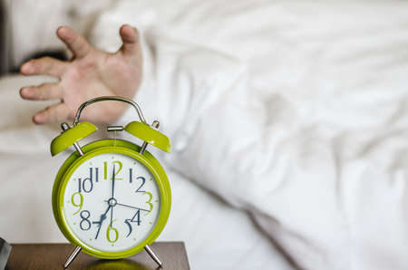 sleeping asian young male disturbed by alarm clock early morning on bedの写真素材