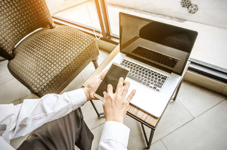 young man working from coffee shop using smart phone and notebook computer, man's hands using smart phone in interior.の写真素材