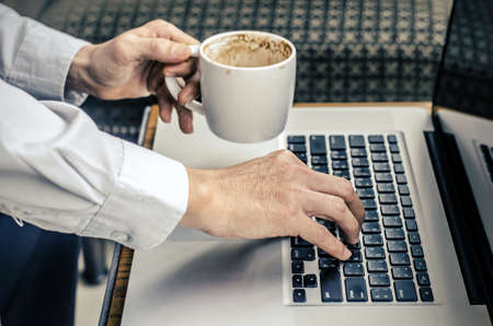 man with a cup of coffee working on his laptopの写真素材