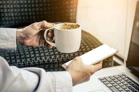 Young hipster guy texting with his mobile phone at the bar and having a cappuccino.Young man drinking espresso coffee in city cafe during lunch time and working on tablet computerの写真素材