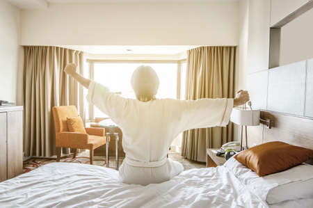 A young man waking up in bed and stretching his armsの写真素材